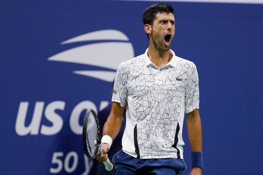 A male tennis player in a white shirt cries out while looking to his left with his arms by his side.