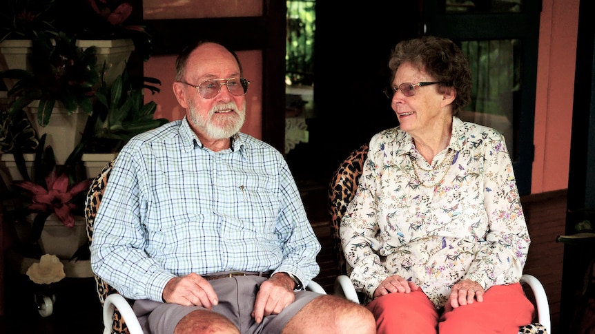 Two people in their 80s sit on a verandah, neither looks directly at the camera