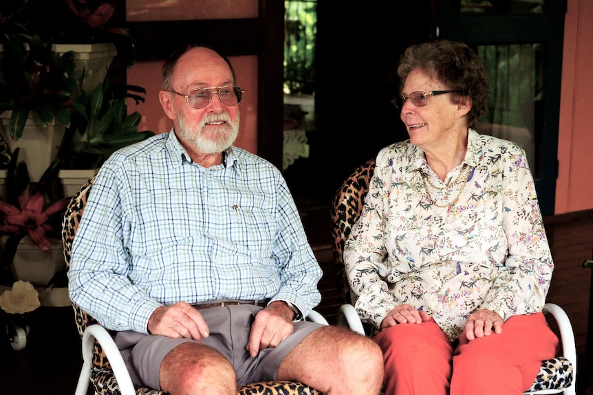 Two people in their 80s sit on a verandah, neither looks directly at the camera