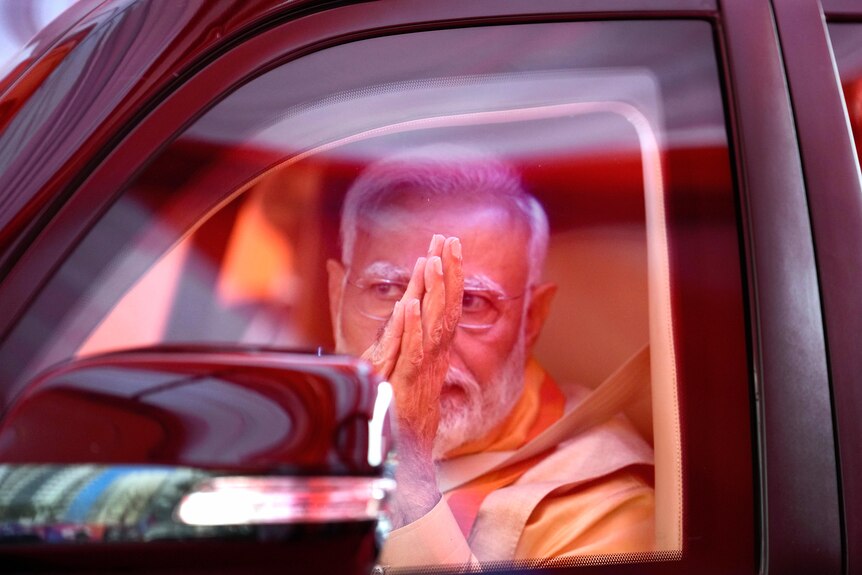 Narendra Modi, seen through a car window, brings his hands together in prayer