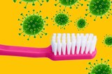 a pink toothbrush against a yellow background with green virus particles around it