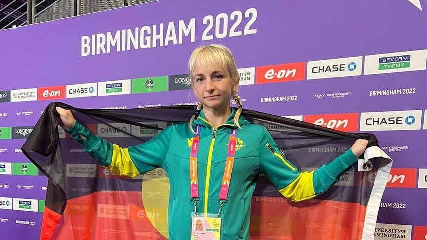 a photo of a woman holding a flag, in commonwealth games uniform 