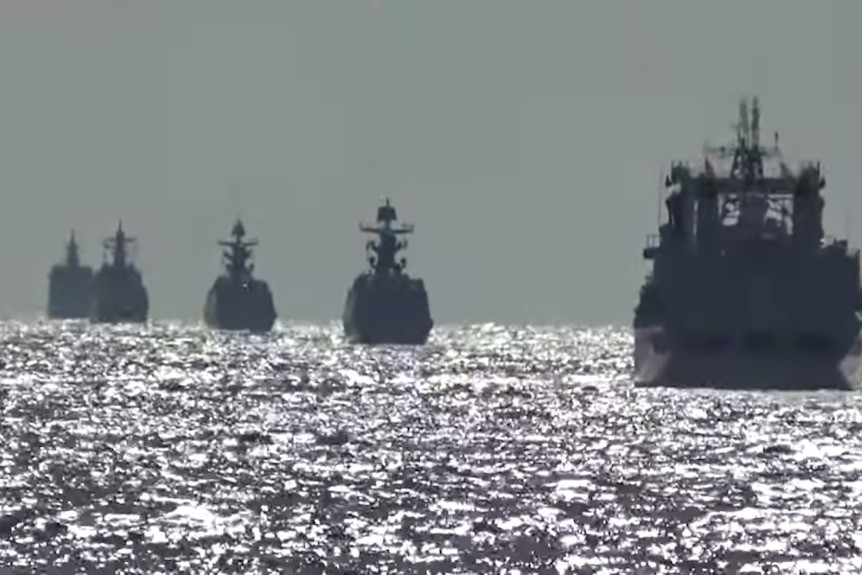 A silouhette shot of six ships sailing away from the camera at dusk