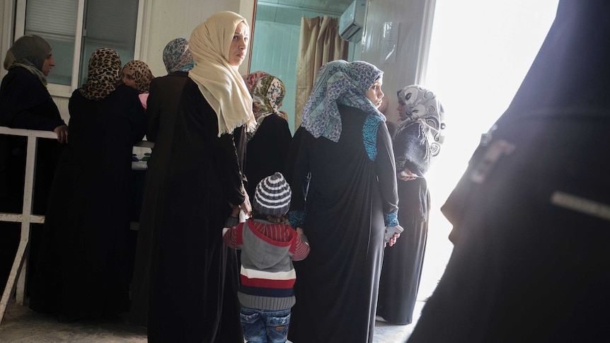 Women hold hands with a child in the Zaatari camp outside a room in the medical clinic.