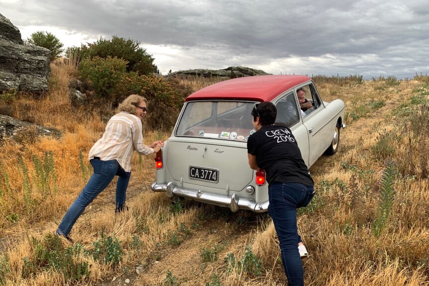 Two women pushing old Austin car up a hill.