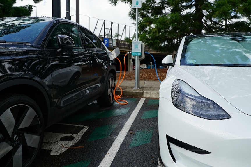 A white Tesla and black Volvo plugged into an electric vehicle charging station in Brisbane