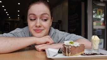 Phoebe Clarke leans on a table and looks at a piece of cake.