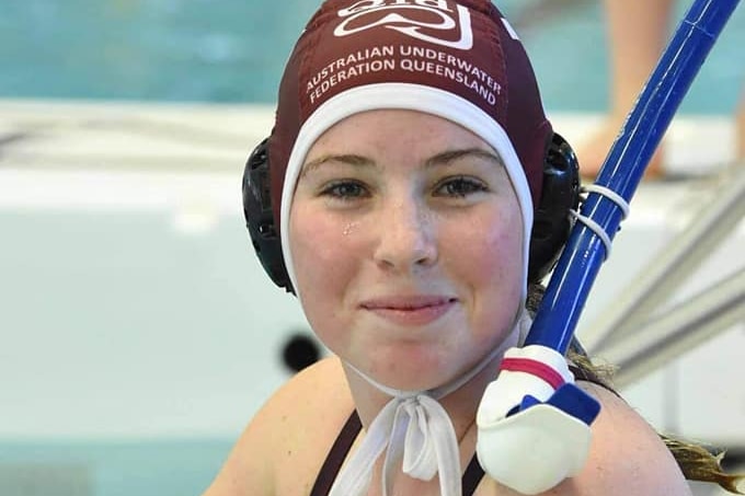 Sarah Hartley cleaning out her mask in the pool wearing the Australian Underwater Association Queensland helmet.