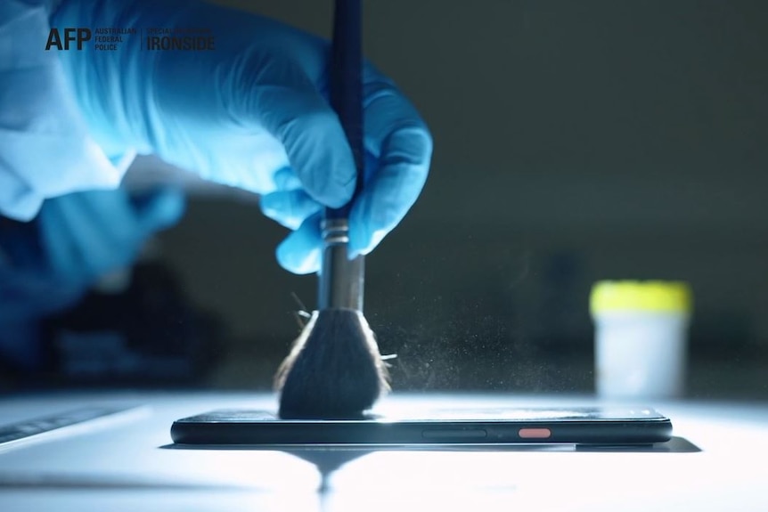 an investigator wearing plastic gloves dusting off a mobile phone for finger prints
