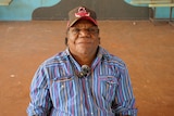 An Aboriginal man wearing a cap and stripey shirt.