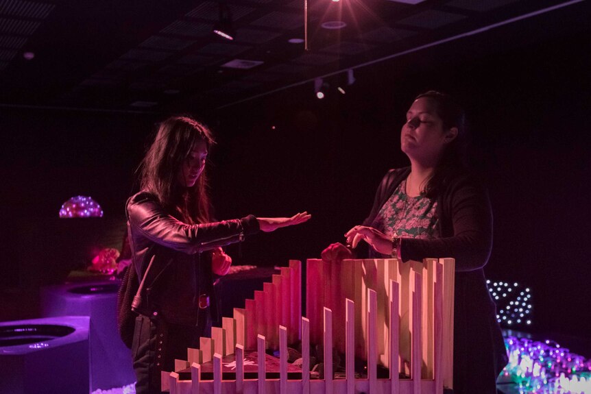 Two young girls hover their hands over an interactive art installation.