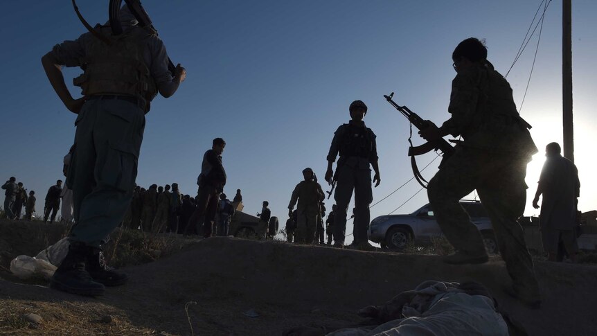 Afghan security forces stand over a body of a Taliban militant