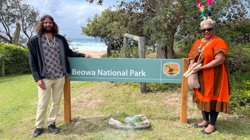 Man and a woman standing on either side of a 'Beowa National Park' sign.
