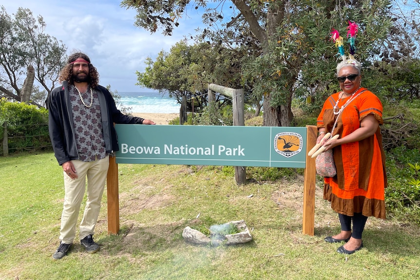 Man and a woman standing on either side of a 'Beowa National Park' sign.