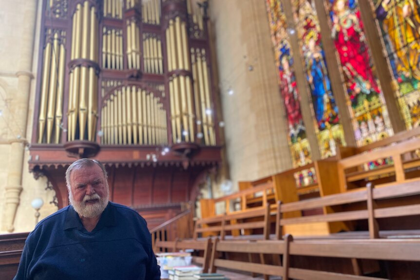 An older, bearded man in a cathedral with a huge organ behind him.