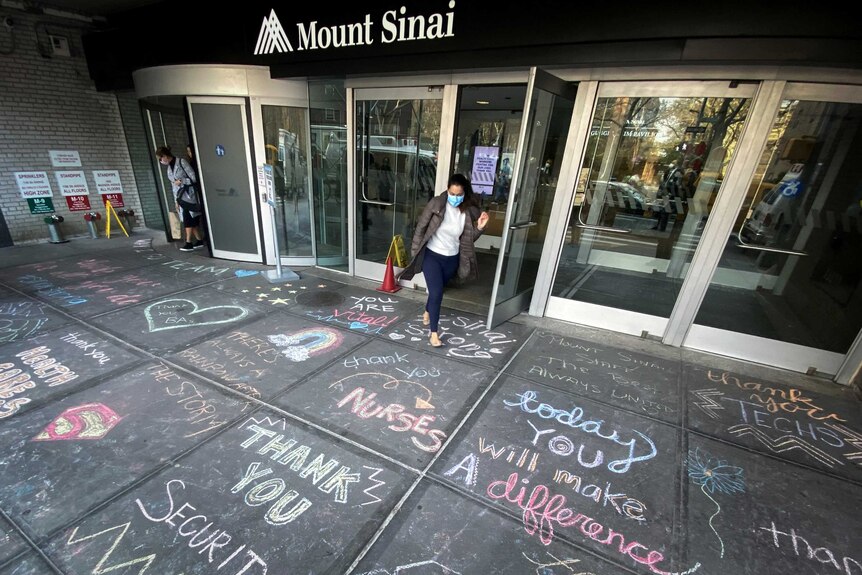 A woman exits Mount Sinai Hospital in Manhattan past messages of thanks written on the sidewalk