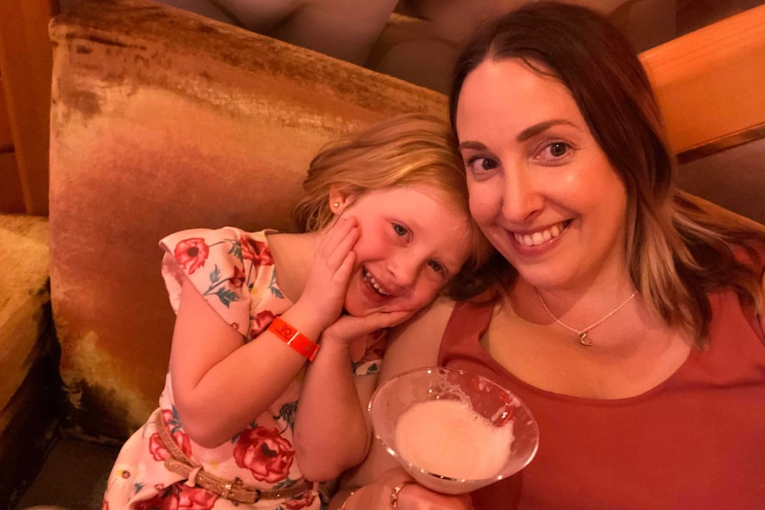 Karina Rogers holding a cocktail, with her daughter on the Voyager of the Seas leaning on cushions