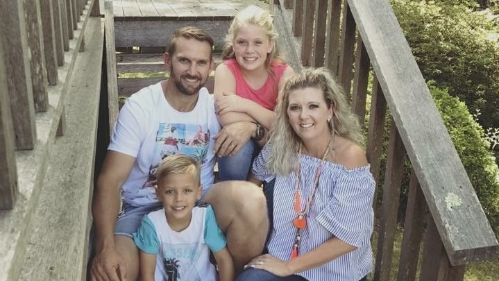 Angela, Brenden and their two children sit smiling on the steps