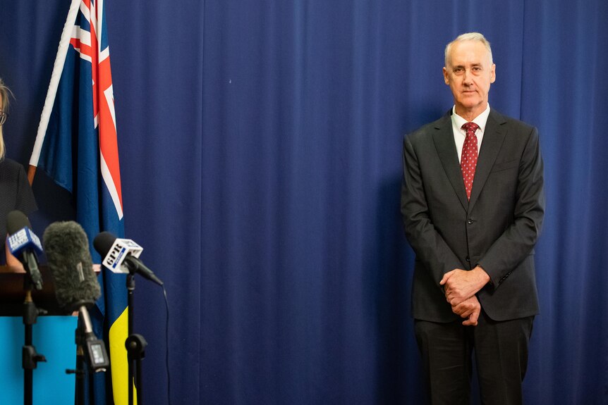 A man standing in front of a blue curtain at a press conference