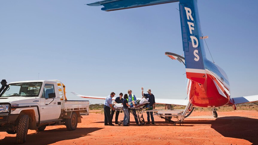 A patient is loaded into a plane parked on a red dirt runway. 