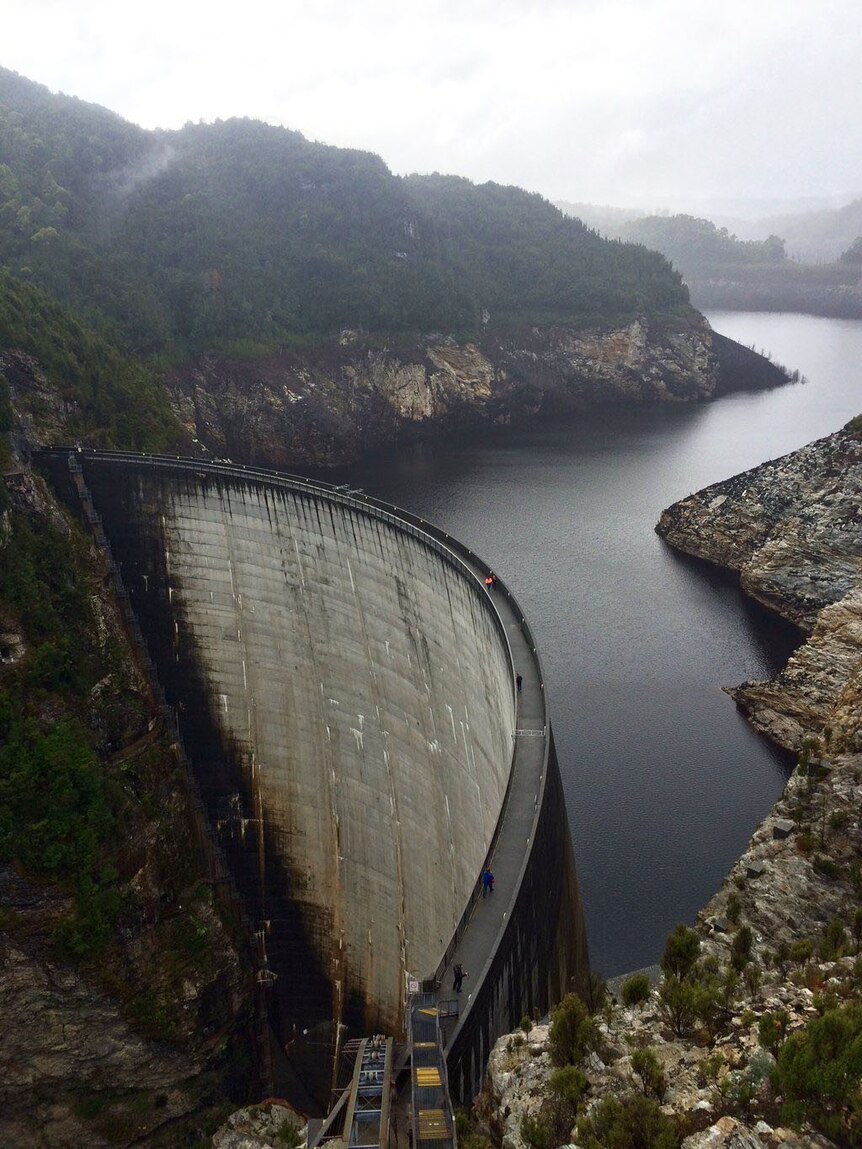 An aerial photo of a dam wall holding back dark water.