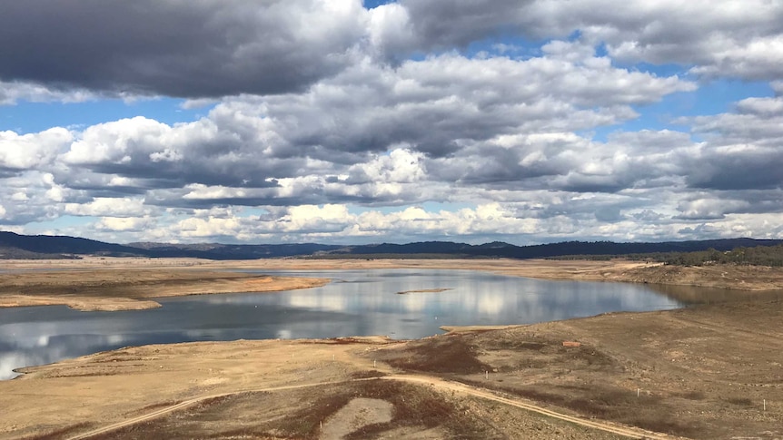 A dry bed of a dam with ponds of water in the background.