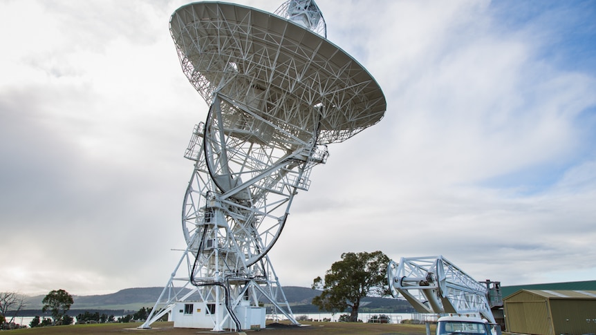 A man stands in front of a large radio telescope in Tasmania.