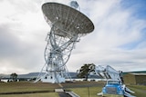 A man stands in front of a large radio telescope in Tasmania.
