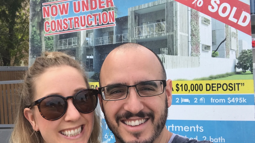 Woman and man stand smiling in front of a sold property sign.