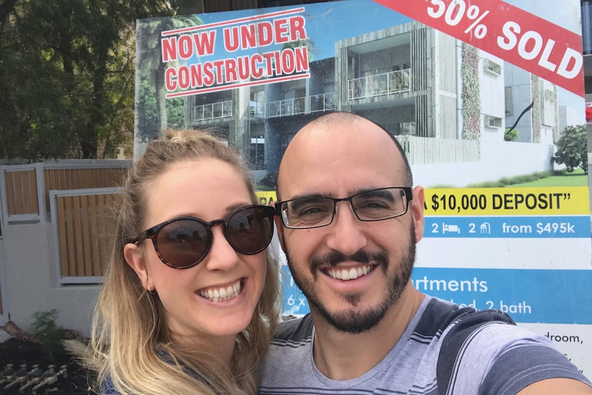 Woman and man stand smiling in front of a sold property sign.