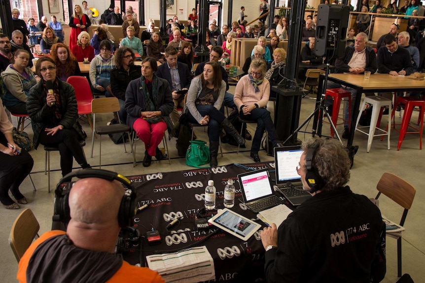 A woman speaks into a microphone as a crowd watches a radio broadcast