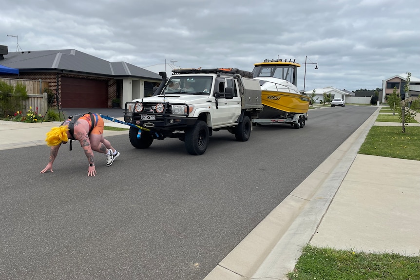 A strongman pulls a landcruiser and boat while tethered to them by a chord