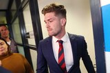 Melbourne player Tomas Bugg, dressed in a suit and tie, looks glum as he leaves the tribunal.