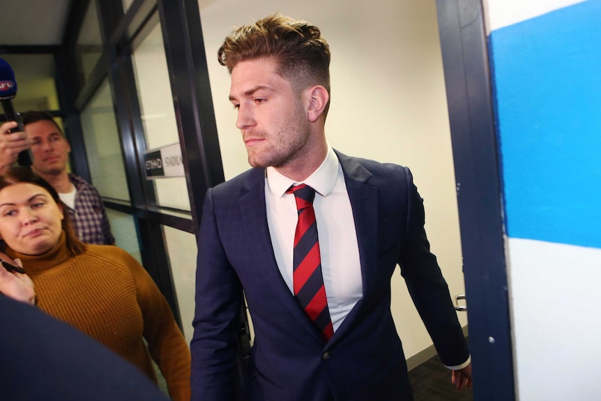 Melbourne player Tomas Bugg, dressed in a suit and tie, looks glum as he leaves the tribunal.