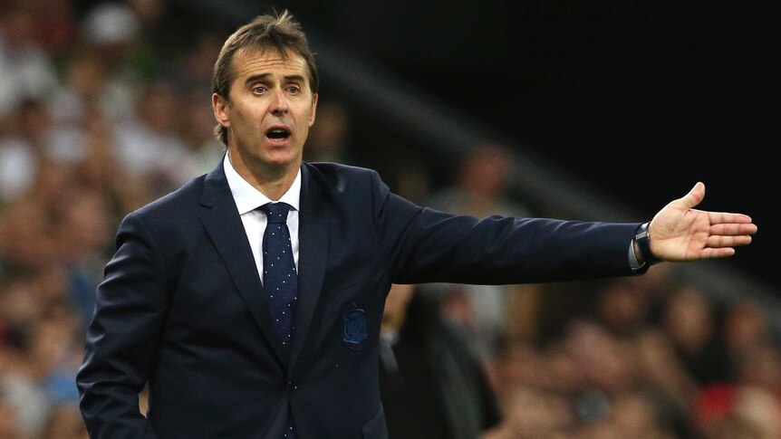 Julen Lopetegui, stands with a stunned expression on his face with one arm out stretched with a crowd on bleachers behind him