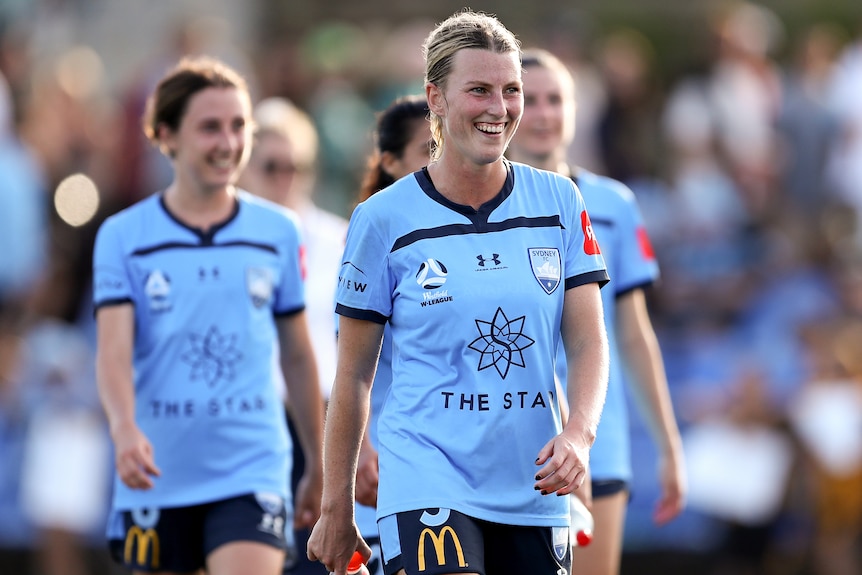 Ally Green smiles wearing a blue football kit, leads other players onto the pitch