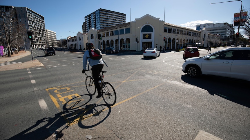 A cyclist riding straight on Tourist Drive onto London Circuit, past the Melbourne Building. 