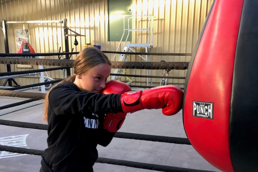 A young teenaged girl punches a boxing bag