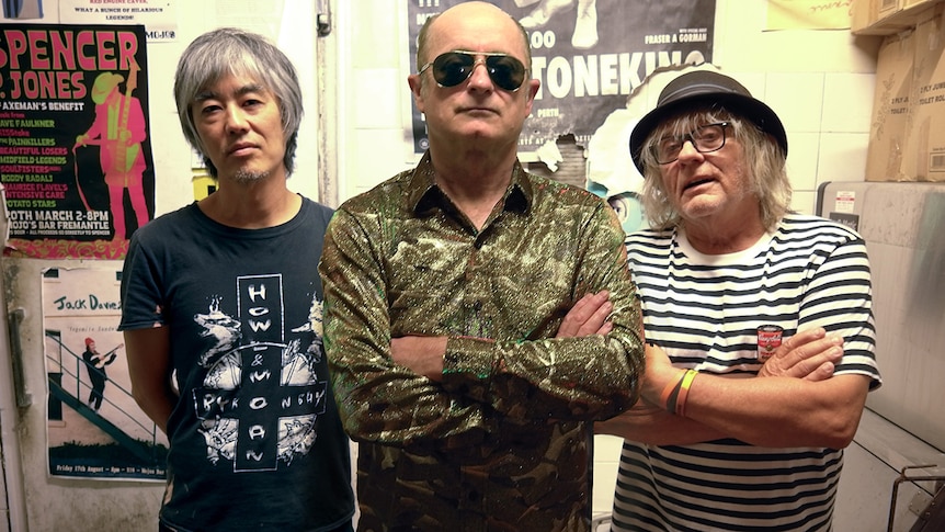 Ray Ahn, Dave Faulkner and James Baker of The Victims stand side by side in a backstage dressing room