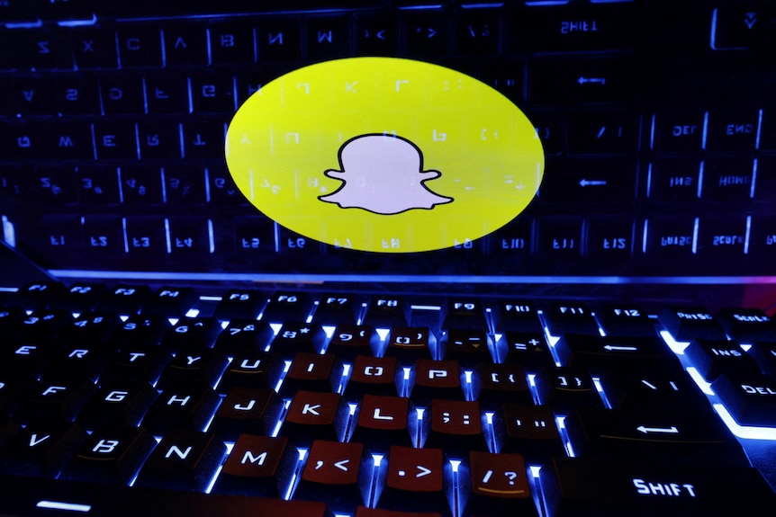 A yellow Snachat logo is superimposed on a dark, shiny computer keyboard.