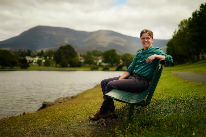 Rowan Richard sits in a park in Hobart with a mountain in the background.