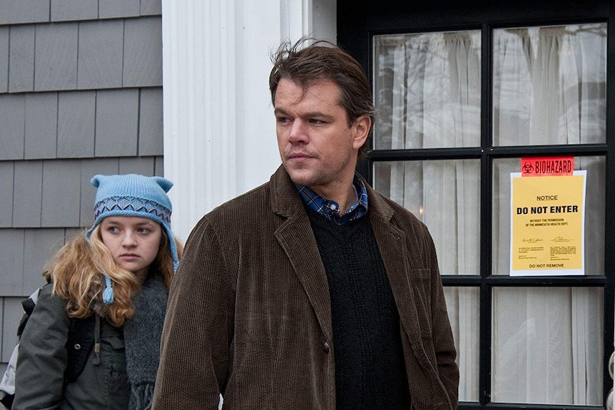 Matt Damon and a young girl walking past a door with a 'biohazard' sign on the front