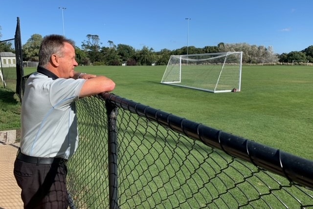 A man standing looking out at soccer goals and pitch 