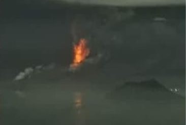 Lava flows from the top of a volcano, which is surrounded by water.