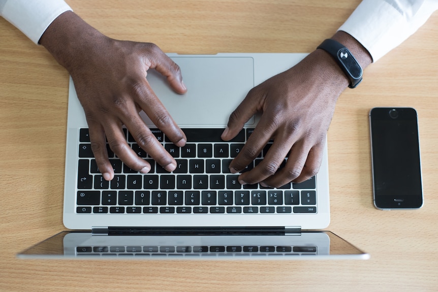 A pair of hands using a laptop. A smartphone sits next to the laptop.