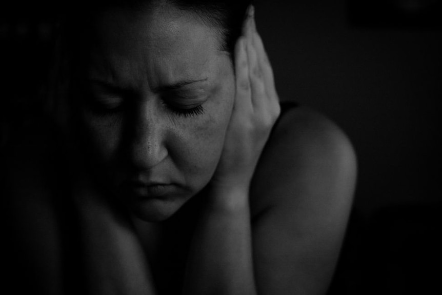 Black and white photo of a woman with her eyes closed and her hands over her ears