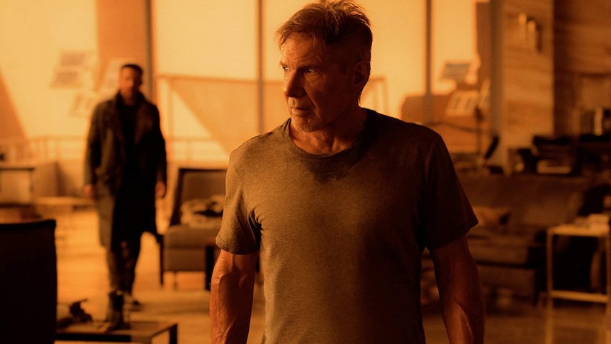 Still image from 2017 film Blade Runner 2049 of actor Harrison Ford walking away from Ryan Gosling inside a home at sunset.
