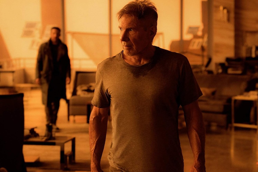 Still image from 2017 film Blade Runner 2049 of actor Harrison Ford walking away from Ryan Gosling inside a home at sunset.
