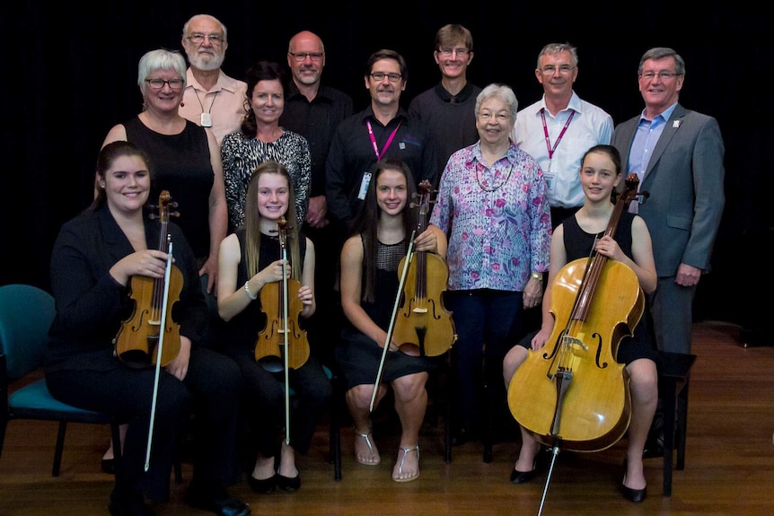 A group of people on a stage with four young women in the front with quartet instruments