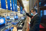 New York Governor Andrew Cuomo, wearing a face mask, waves at people inside the New York Stock Exchange.